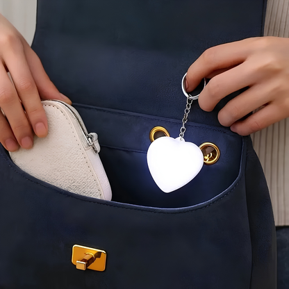 Heart-shaped keychain light being placed into a dark blue handbag.